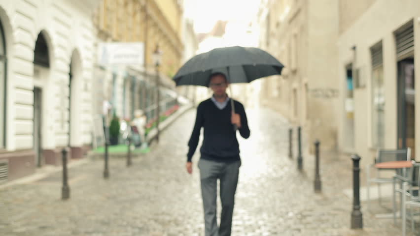 Young man with umbrella and phone walking on the street
