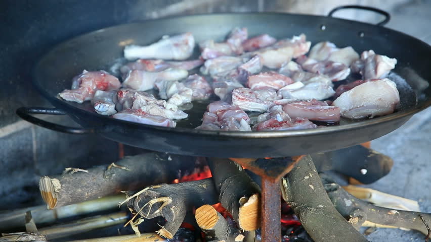 preparing large dish of paella with firewood, frying chicken