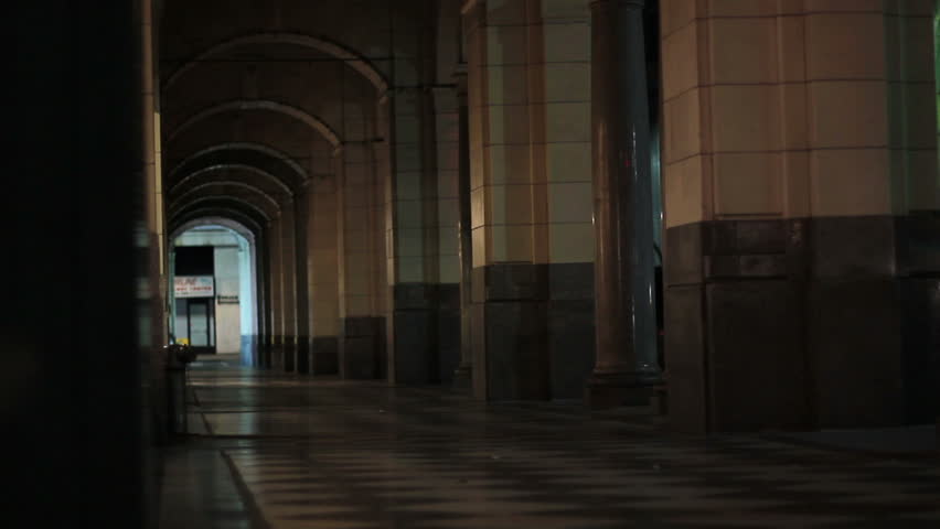 A man walks down a dark arched pathway at night alone