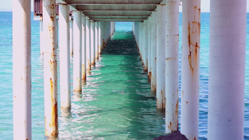 A still shot of the turquoise water and the pillars under the boardwalk down at the ocean.