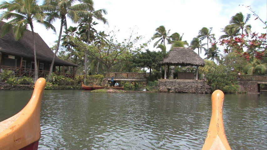Polynesian canoes in a tropical pool in Oahu, Hawaii. Palm trees and tropical huts. Polynesian Cultural Center, Hawaii number one tourist attraction. Show the various islands of Polynesia. 