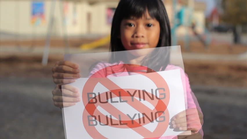 A cute Asian girl holds up a large "NO BULLYING" sign on the school playground.