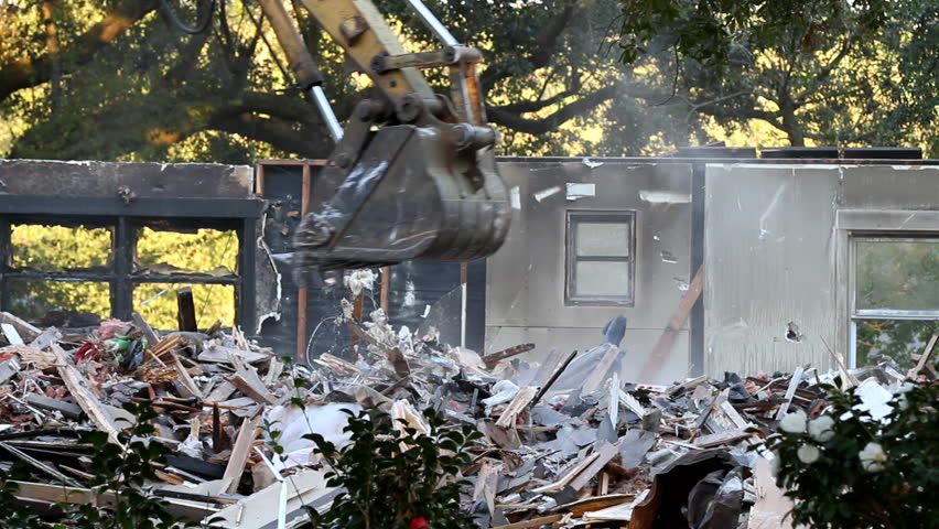 Excavator bucket shove is used to pick up debris as it demolishes an old abandoned house to make way for new development.