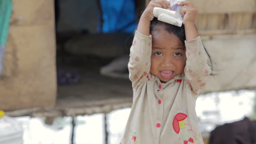 Cambodian kid holding money in slum, shacks at background