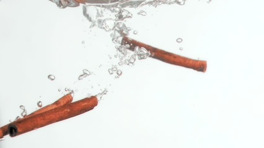 Three cinnamon sticks in a super slow motion falling in the water against a white background