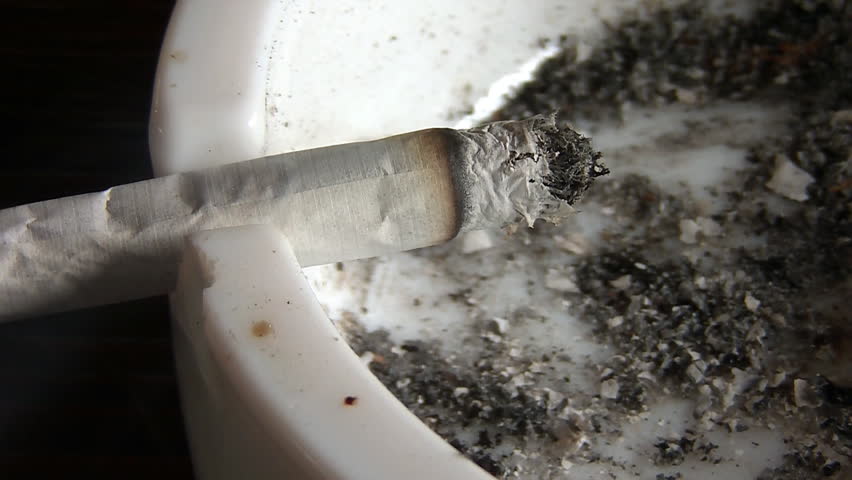 Cigarette burning in a filthy ashtray 
