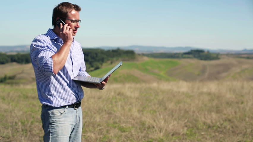 Young architect with laptop and cellphone on meadow, crane shot
