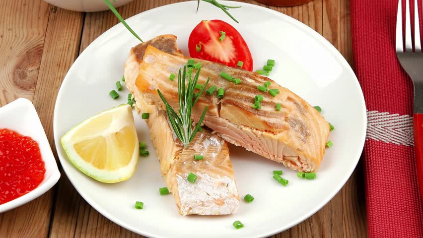 savory fish portion : roasted norwegian salmon chunks with lemon and vegetable salad rosemary twig and red caviar in white bowl over wooden table