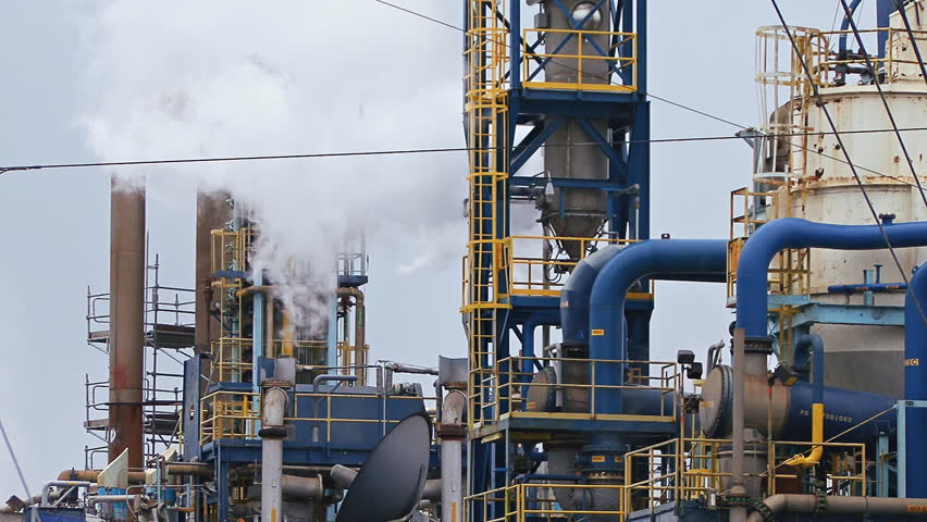 Tighter shot of a large factory industrial plant with many tubes, pipes, and steaming vents on a grey, sullen day.