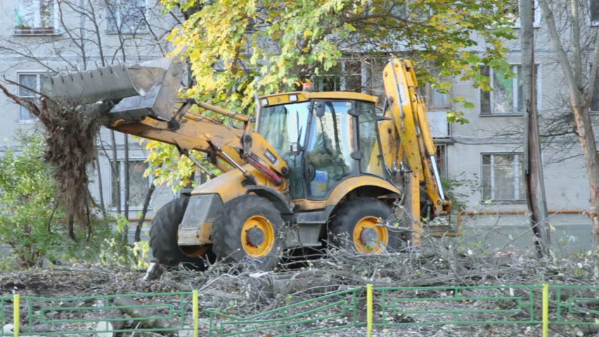 Excavator ride backward with part of wood near dwelling house at autumn day