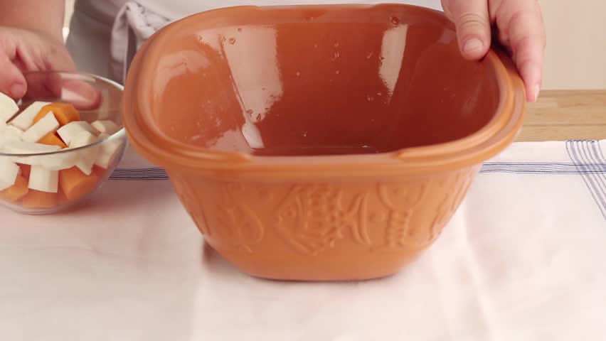 Root vegetables being added to a terracotta baking dish