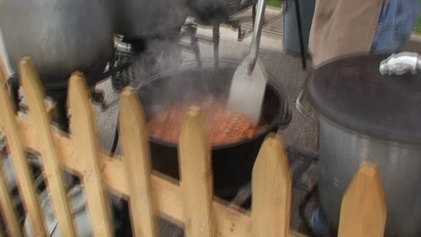 Person stirring a large pot of chili at a fair