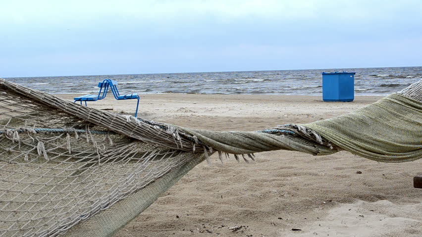 fence made of fishing net move in wind. beach decor bench and waste bin.