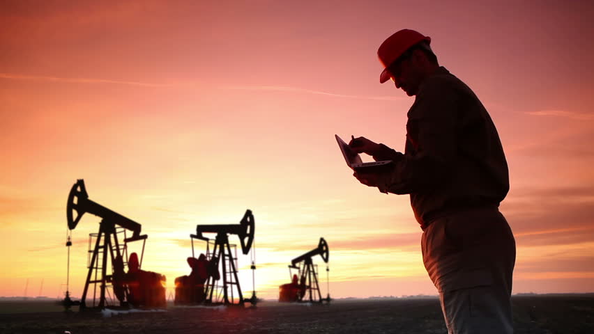 Oil Industry Pump jack with one oil worker who using a phone and typing on laptop.In a background are Silhouettes of three Pump jack at sunset light.