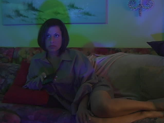A beautiful young woman wearing a man's oversize button-down shirt, appears to be irritate and angry because she can't find something worthwhile to watch on late-night television.