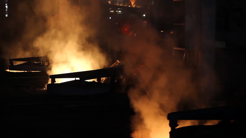 Hard work in the foundry, worker controlling iron smelting in furnaces, too hot and smoky working environment
