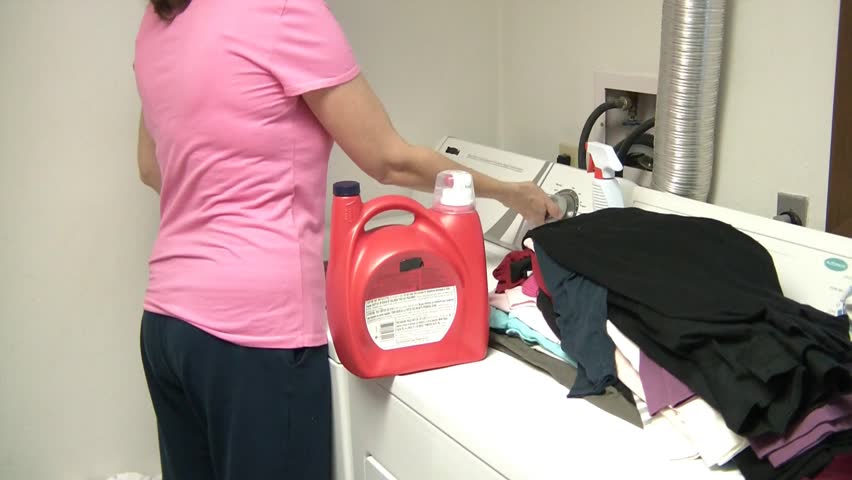 Woman washing clothes with detergent in laundry room.