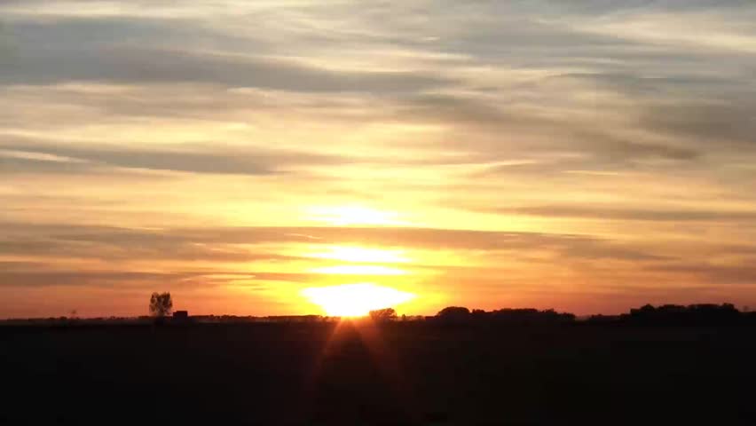 Time lapse of colorful dusk at days end revealing brilliant yellow and orange colors with jet exhaust as sun sets behind clouds.