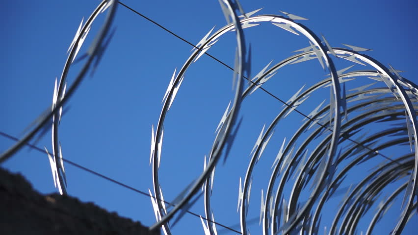A close up, dolly shot of razor wire glistening in the sun against a blue sky.