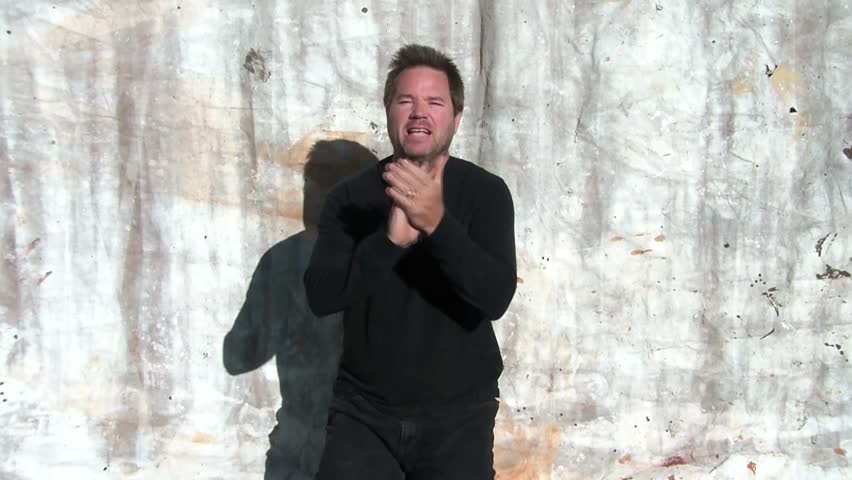 Man claps with approval nodding intermittently with emotion, in sunlight wearing black with canvas backdrop.