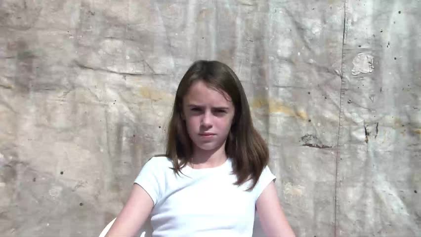 Girl gestures a bad smell with her hand by waving it back and forth in front of face and acts gagging, in sunlight with backdrop.