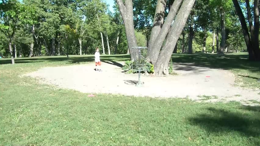 Father and two children play with sport disc in sunlight and attempt to throw discs into metal chains on goal.