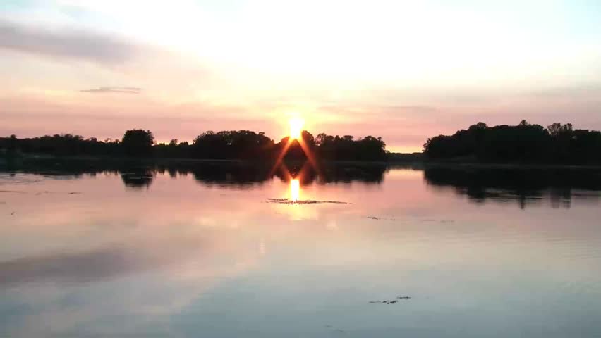 Calm sunset over pristine lake for the first part of clip, and then rocks are thrown randomly onto placid water leaving behind wakes in the aftermath.