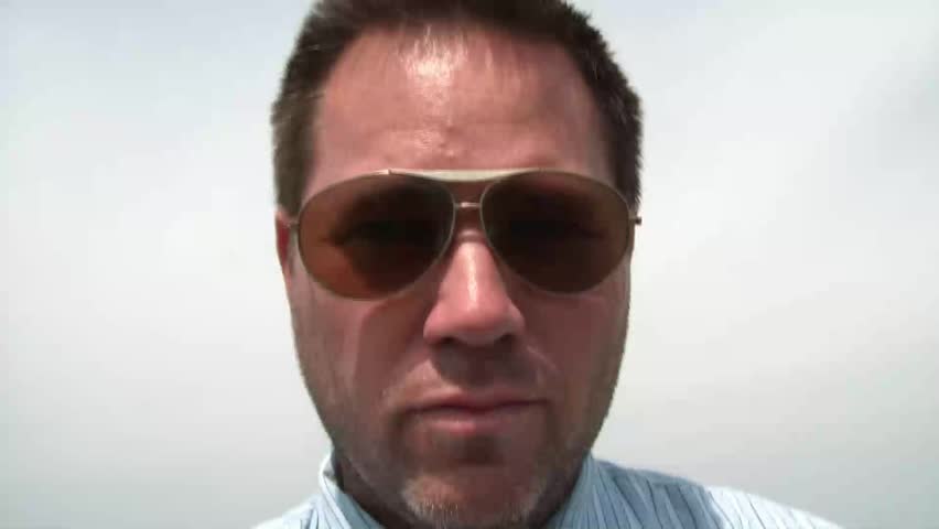 Businessman with sunglasses on in bright sunlight calls out various women presumably by whistling with fingers, gestures to approach him, and tilts glasses down.