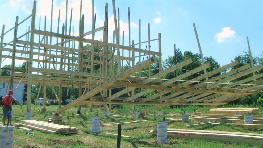 Carpenters work to help put bent in place on foundation while raising a barn. 