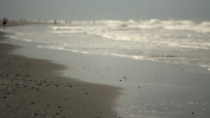 Waves wash up on shore on Isle of Palms (near Charleston, SC) in early morning low light. People walking on beach out of focus in distant background. Nat sound.