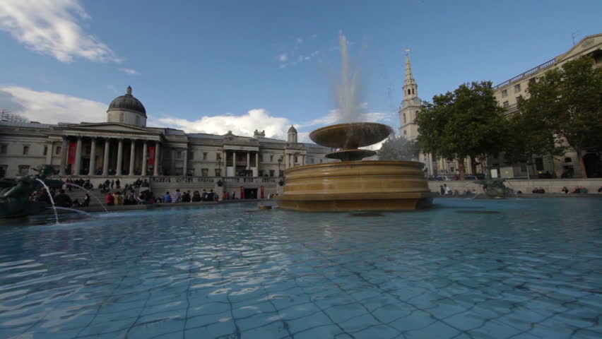 A stationary shot of National Gallery (London) seen from a fountain. People are on the stairs and buildings on the right of the scene. 