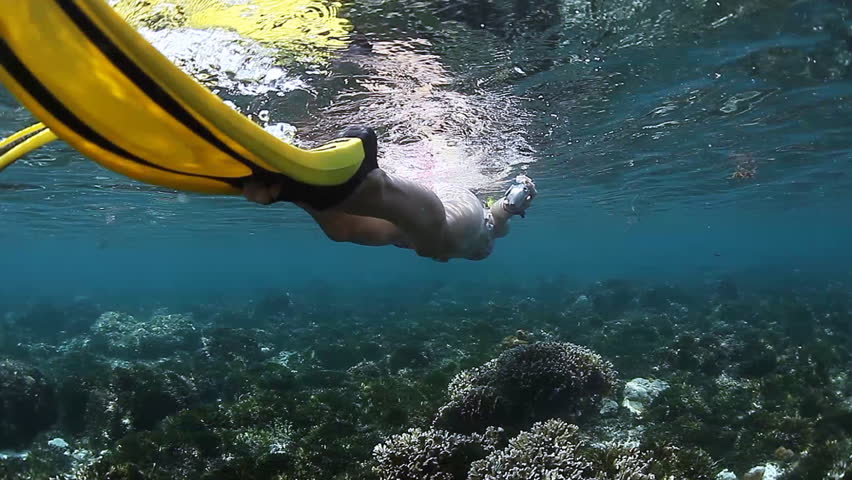 Underwater scene with young lady finning over coral reef in a tropical sea