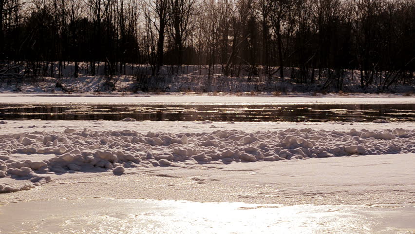 Frozen Neris river in winter and floe floating in water and sun reflections on it.