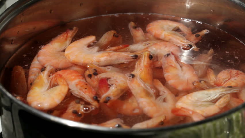 Shrimp are simmered in a saucepan. Men's hand throws new shrimp.