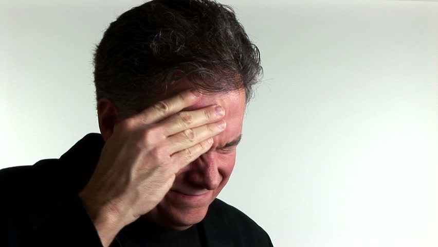 A man suffering from a migraine headache stops and looks at the camera.