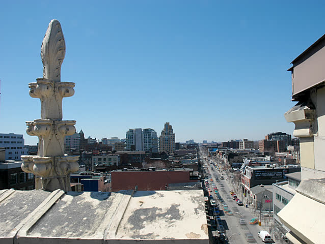 Time-lapse in city of rooftop spire and moving shadow, balanced by heavy road traffic in lower-right.