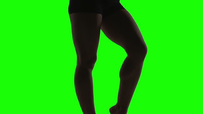 Silhouette of a young woman dancing in front of green screen, legs
