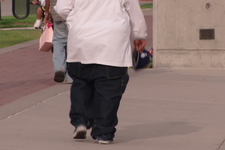 An overweight man walking down urban street.
