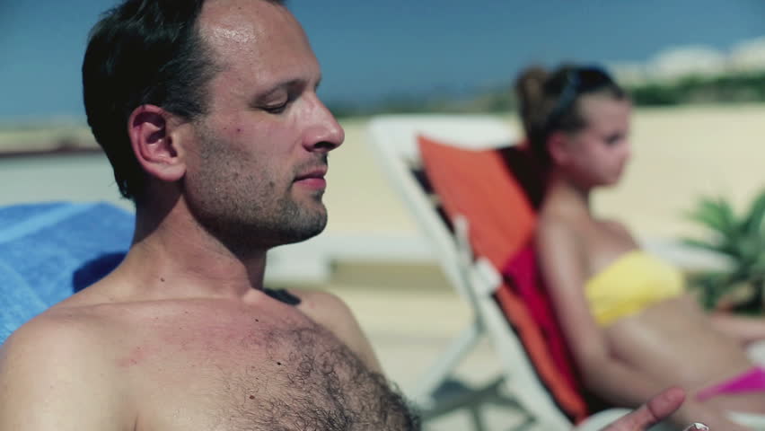 Young man lying on sunbed and applying sun cream
