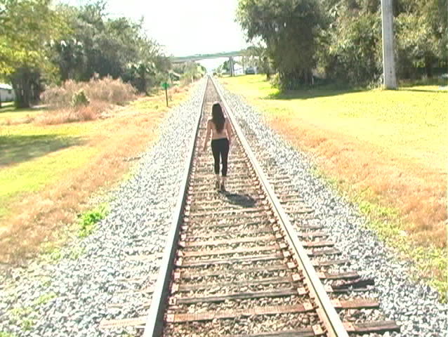 A girl walks away from the camera on a long stretch of railroad track.  Camera cranes up with a slight tilt.  Can be used alone or as a frame-accurate extension of 1a.