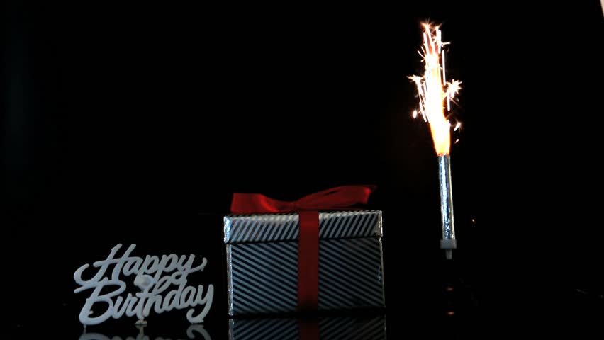 Sparkler burning beside gift and happy birthday sign on black background