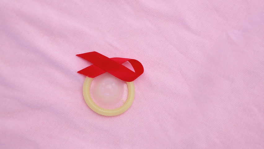 Condom and red ribbon on revolving pink blanket