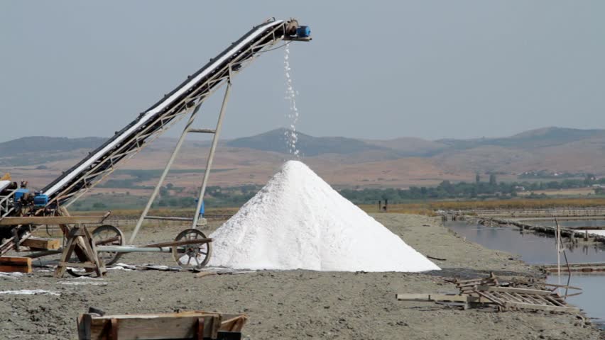 Heap of sea salt crystals under conveyor belt. Traditional salt-production process in a saline refinery plant near Burgas in Bulgaria.