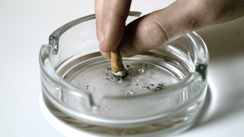 Hand extinguishing cigarette in empty ashtray in slow motion