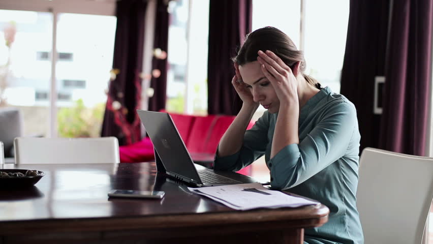Overwhelmed, sad businesswoman with documents and laptop in home

