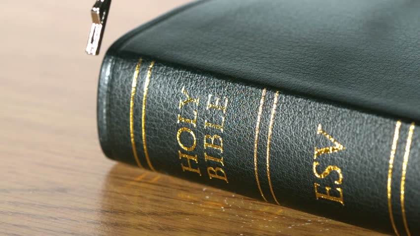 Rosary beads falling onto bible on a table in slow motion
