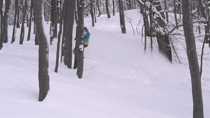 SLOW MOTION: snowboarder doing powder turn in forest