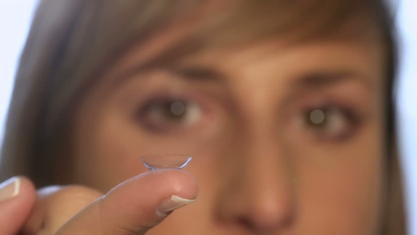Young woman holding contact lens on a finger and inserts it into her eye.