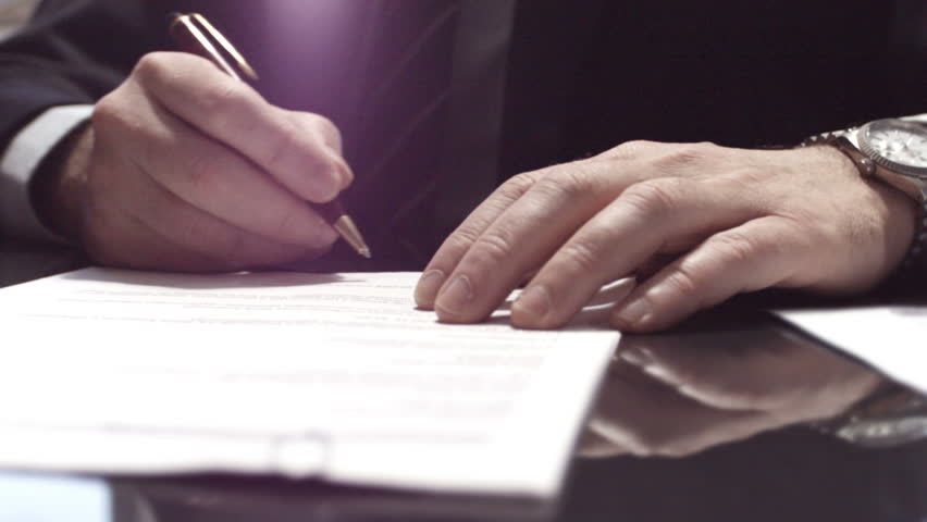 Businessman sitting at shiny office desk signing a contract with noble pen
