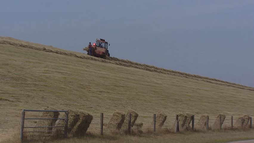 Farmer haying at sea dike, square bales rolling down. The Hondsbossche and Pettemer Zeewering  is a 5,5 km long sea dike in The Netherlands.